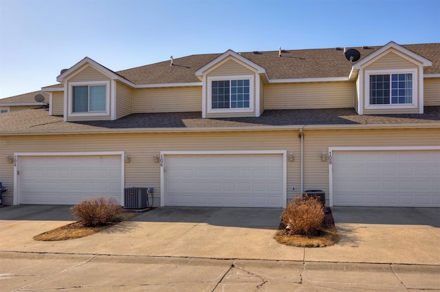 view of front of property featuring driveway, a shingled roof, a garage, and central AC unit