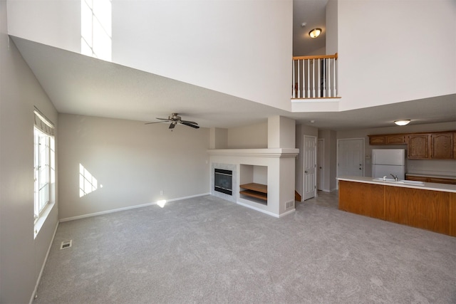 unfurnished living room featuring ceiling fan, light carpet, a towering ceiling, visible vents, and a tiled fireplace