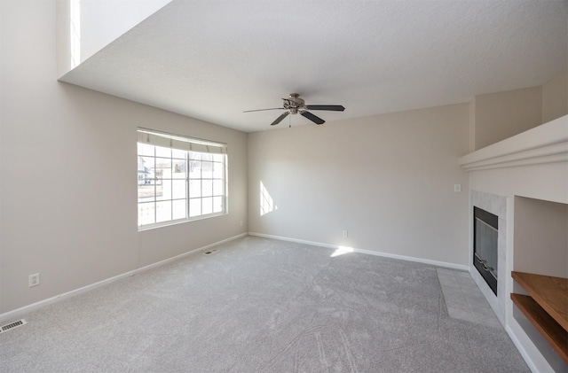 unfurnished living room with carpet floors, visible vents, a tiled fireplace, ceiling fan, and baseboards