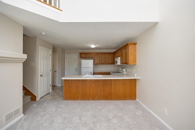 kitchen with a peninsula, white appliances, a sink, visible vents, and light countertops