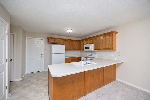 kitchen with white appliances, brown cabinets, a peninsula, light countertops, and a sink