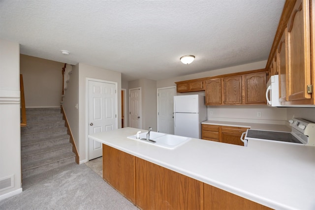 kitchen featuring a peninsula, white appliances, brown cabinets, and a sink