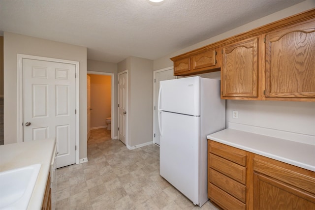 kitchen with a sink, light countertops, freestanding refrigerator, light floors, and brown cabinetry