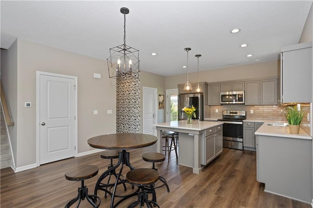 kitchen with gray cabinetry, decorative backsplash, decorative light fixtures, a kitchen island, and stainless steel appliances