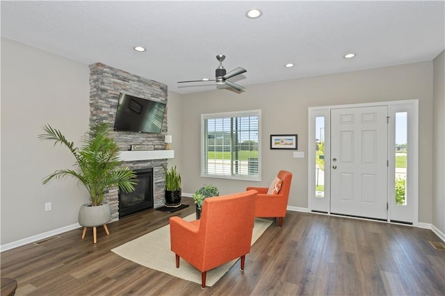 living room with ceiling fan, a stone fireplace, and dark wood-type flooring