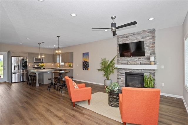 living room featuring a stone fireplace, ceiling fan, and dark hardwood / wood-style floors