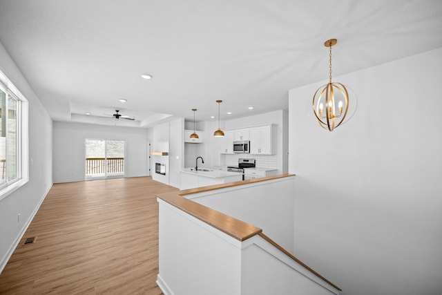 kitchen with sink, stainless steel appliances, a raised ceiling, pendant lighting, and ceiling fan with notable chandelier