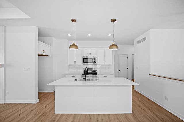 kitchen with appliances with stainless steel finishes, sink, pendant lighting, white cabinetry, and an island with sink