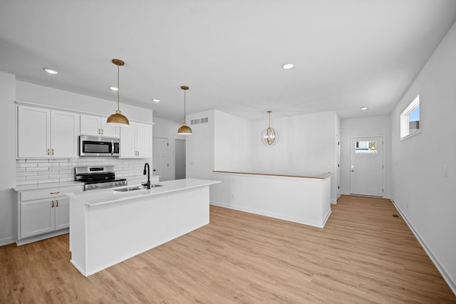 kitchen with appliances with stainless steel finishes, sink, white cabinetry, hanging light fixtures, and an island with sink