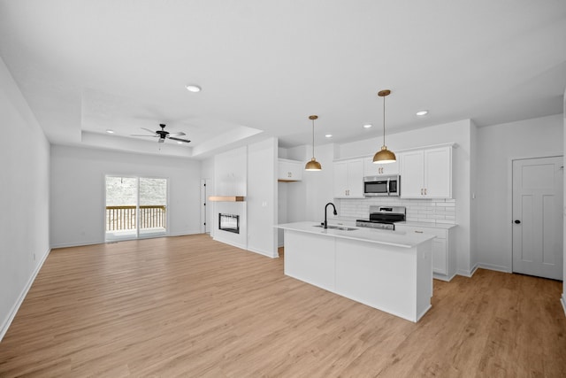 kitchen featuring white cabinetry, sink, a tray ceiling, a center island with sink, and appliances with stainless steel finishes