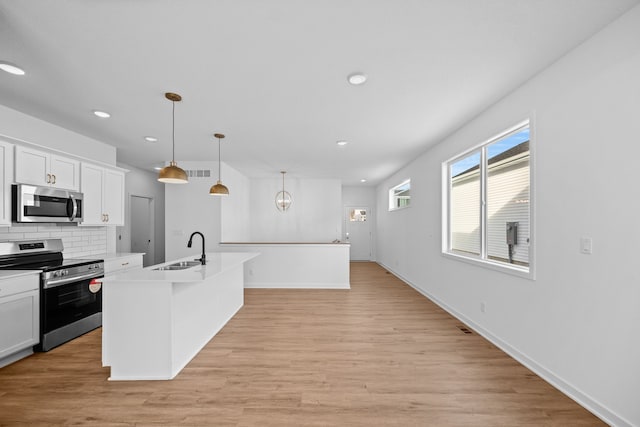 kitchen featuring sink, an island with sink, decorative light fixtures, white cabinetry, and stainless steel appliances