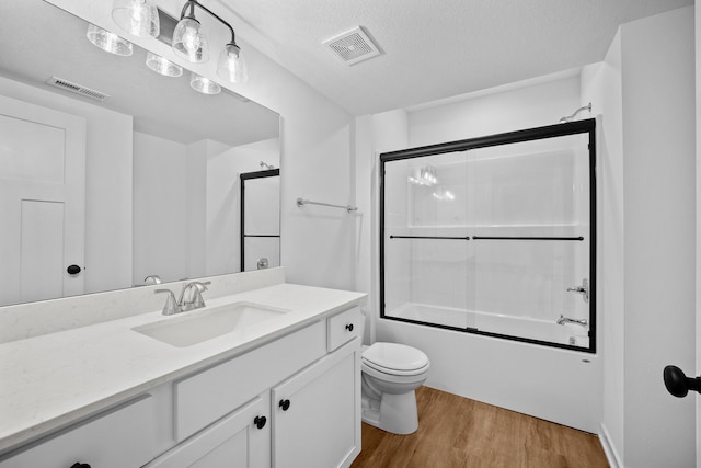 full bathroom with combined bath / shower with glass door, hardwood / wood-style floors, a textured ceiling, toilet, and vanity