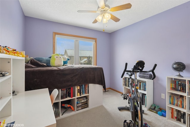 exercise room featuring ceiling fan, light colored carpet, and a textured ceiling