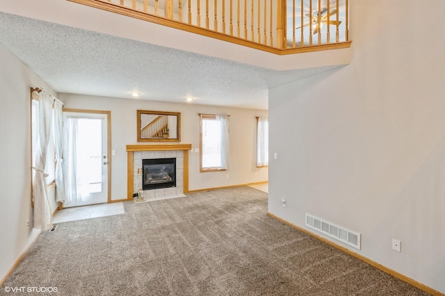 unfurnished living room featuring carpet flooring, a tile fireplace, and a textured ceiling