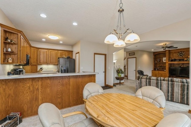 kitchen with ceiling fan with notable chandelier, hanging light fixtures, stainless steel fridge, a textured ceiling, and kitchen peninsula