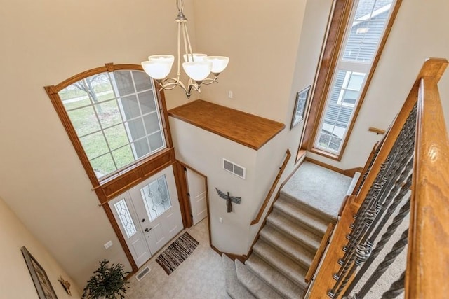 carpeted entryway with a notable chandelier and a towering ceiling