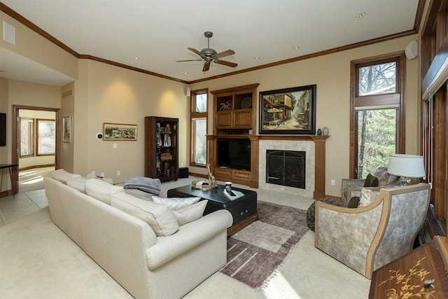 living room featuring a tile fireplace, ceiling fan, crown molding, and light tile patterned floors