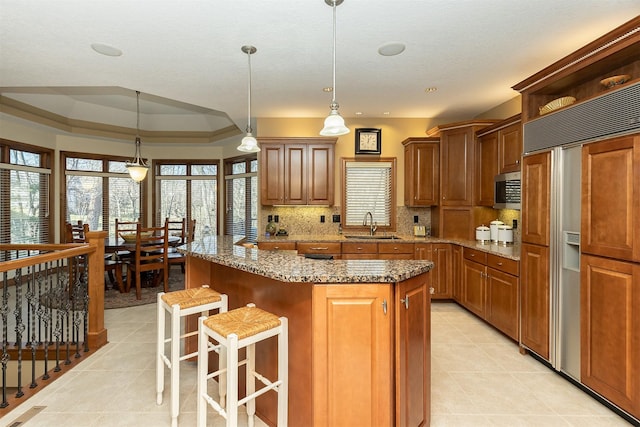 kitchen with hanging light fixtures, a raised ceiling, paneled built in refrigerator, a breakfast bar area, and a kitchen island