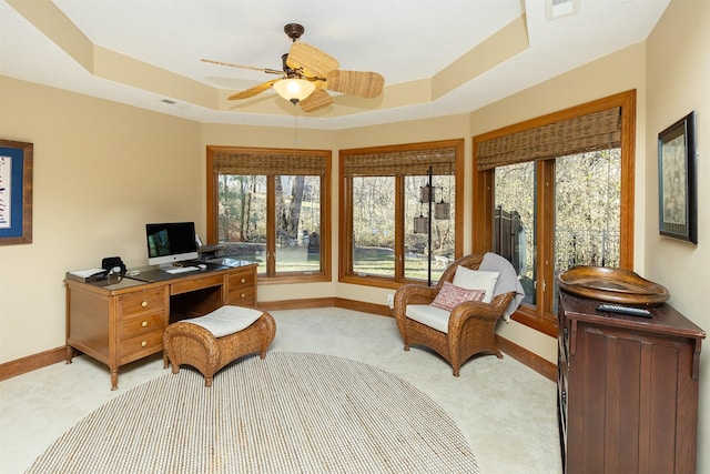 carpeted office featuring a raised ceiling, ceiling fan, and a healthy amount of sunlight