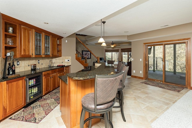 kitchen with a kitchen bar, dark stone countertops, hanging light fixtures, and beverage cooler