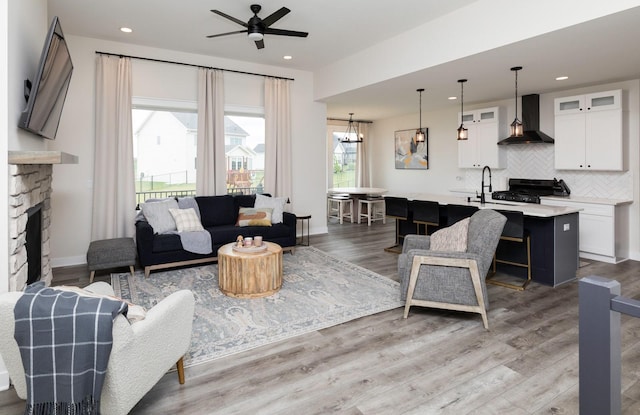 living room featuring a stone fireplace, wood-type flooring, and ceiling fan with notable chandelier