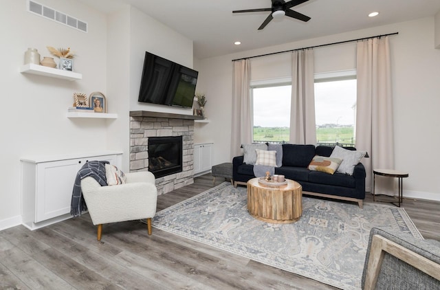 living room featuring hardwood / wood-style floors, a stone fireplace, and ceiling fan