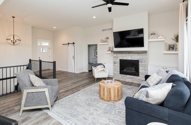 living room featuring ceiling fan with notable chandelier, a fireplace, and light hardwood / wood-style flooring