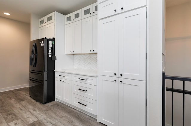 kitchen with decorative backsplash, black refrigerator with ice dispenser, white cabinets, and light wood-type flooring