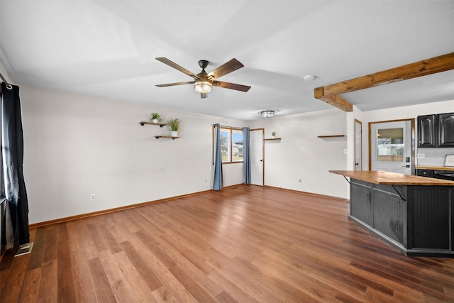 unfurnished living room featuring beamed ceiling, ceiling fan, and dark hardwood / wood-style floors