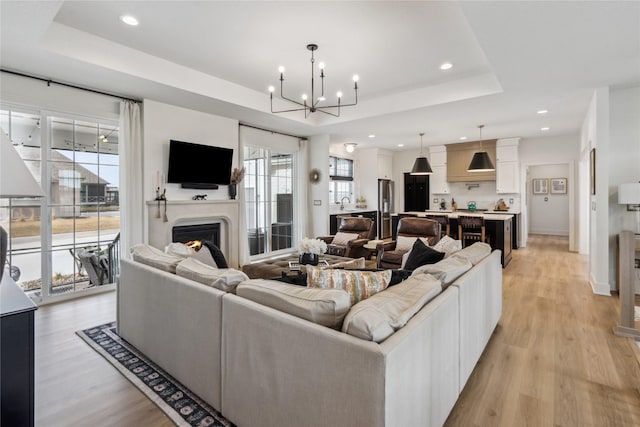 living room with a tray ceiling, sink, a notable chandelier, and light wood-type flooring