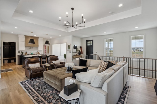 living room featuring a chandelier, light wood-type flooring, and a raised ceiling