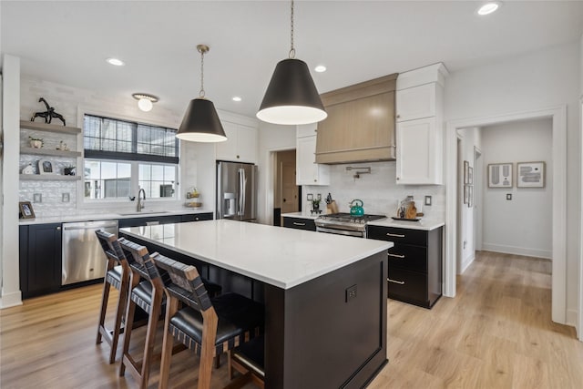 kitchen featuring appliances with stainless steel finishes, sink, white cabinets, a center island, and hanging light fixtures