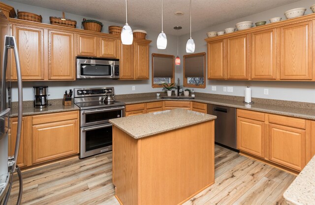 kitchen with sink, a kitchen island, a textured ceiling, and appliances with stainless steel finishes