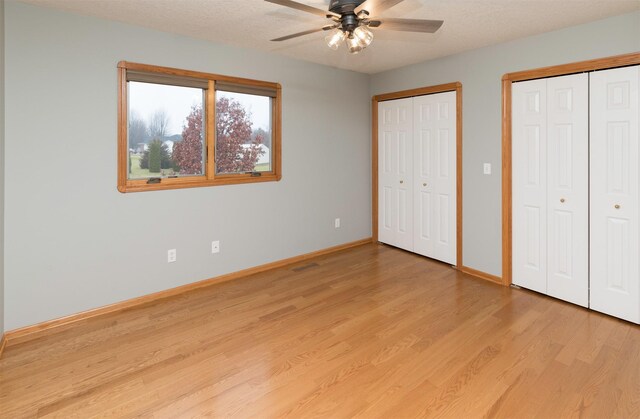 unfurnished bedroom with ceiling fan, light wood-type flooring, a textured ceiling, and two closets