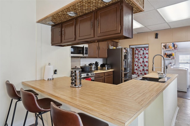 kitchen featuring a kitchen bar, appliances with stainless steel finishes, a drop ceiling, sink, and washing machine and clothes dryer