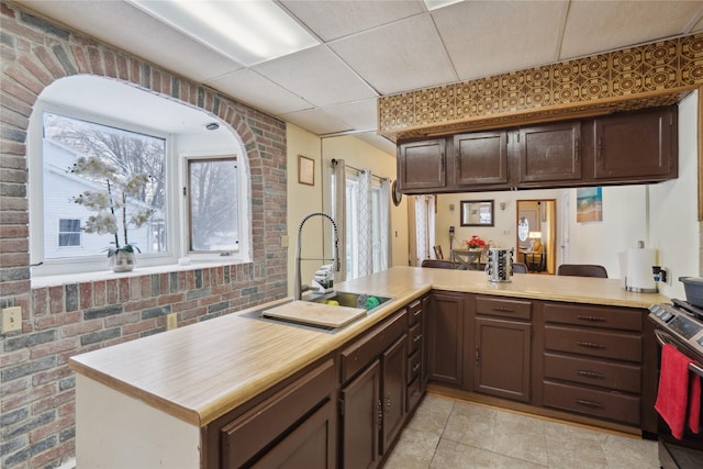 kitchen with a paneled ceiling, kitchen peninsula, sink, and brick wall