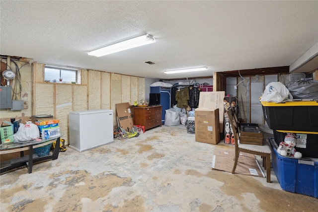 basement with a textured ceiling, electric panel, and fridge