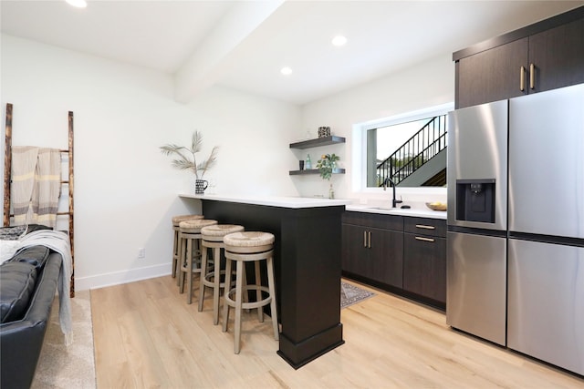 kitchen featuring dark brown cabinetry, light wood-type flooring, beam ceiling, a kitchen bar, and stainless steel fridge with ice dispenser