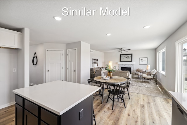 kitchen featuring a stone fireplace, ceiling fan, a kitchen island, light hardwood / wood-style floors, and white cabinetry