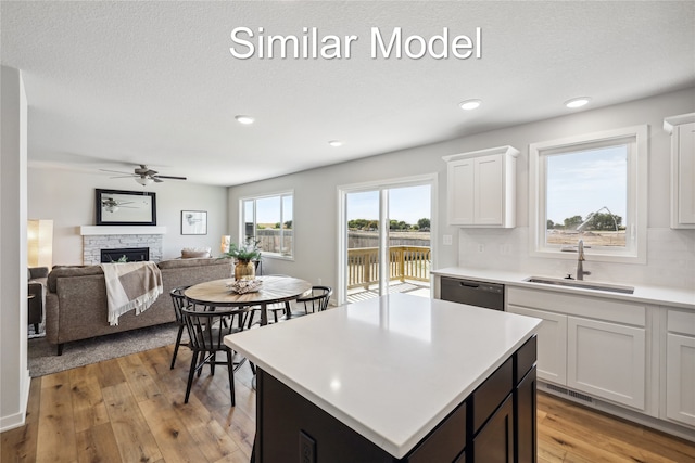 kitchen with ceiling fan, sink, white cabinets, a center island, and a stone fireplace