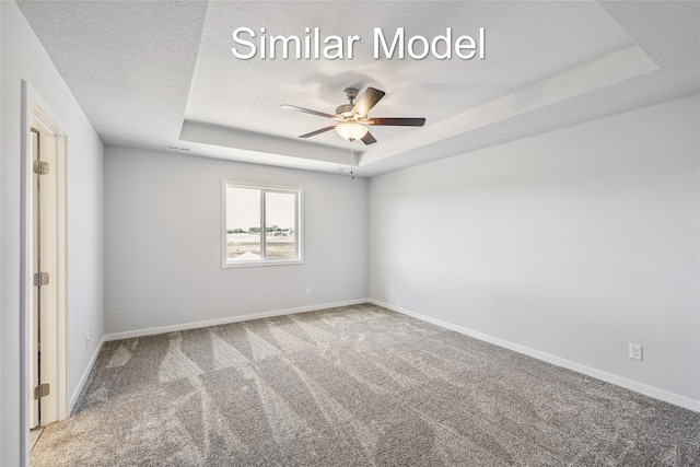 unfurnished room featuring a raised ceiling, ceiling fan, carpet, and a textured ceiling