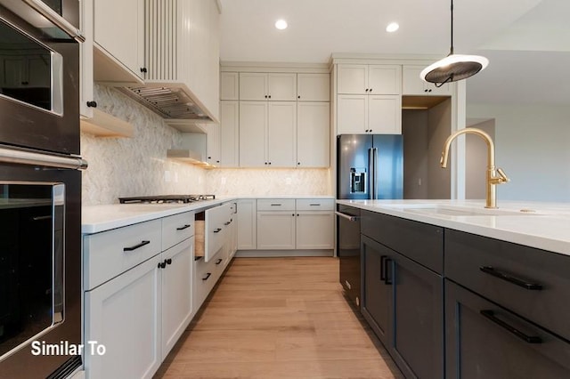 kitchen featuring pendant lighting, white cabinetry, sink, black appliances, and light hardwood / wood-style flooring