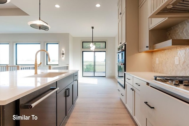 kitchen featuring sink, light hardwood / wood-style flooring, appliances with stainless steel finishes, range hood, and decorative light fixtures