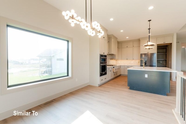 kitchen with hanging light fixtures, a center island with sink, white cabinets, and appliances with stainless steel finishes