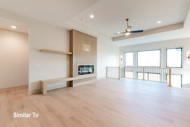 unfurnished living room with a raised ceiling, a large fireplace, ceiling fan, and light hardwood / wood-style flooring