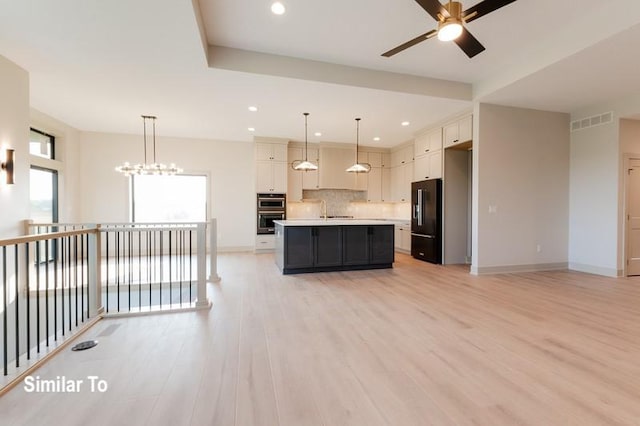 kitchen featuring a kitchen island with sink, hanging light fixtures, white cabinetry, and high end black refrigerator