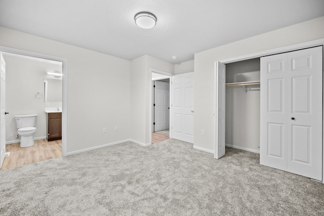 unfurnished bedroom with ensuite bathroom, a closet, and light carpet