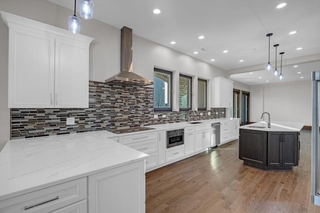 kitchen featuring wall chimney exhaust hood, white cabinetry, light stone counters, hanging light fixtures, and black electric stovetop