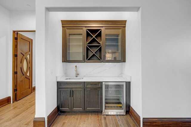 bar featuring sink, dark brown cabinetry, tasteful backsplash, beverage cooler, and light wood-type flooring