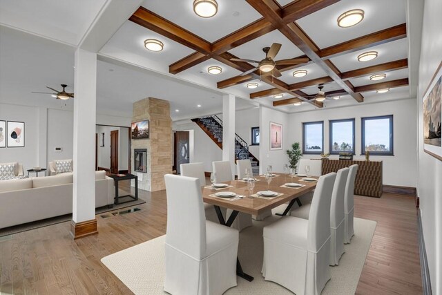 dining space featuring coffered ceiling, a fireplace, beamed ceiling, and light wood-type flooring